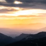 A breathtaking sunrise over a dramatic mountain landscape with a warm glow.