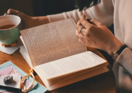 A woman writes in a journal while enjoying a cup of coffee at a wooden table.