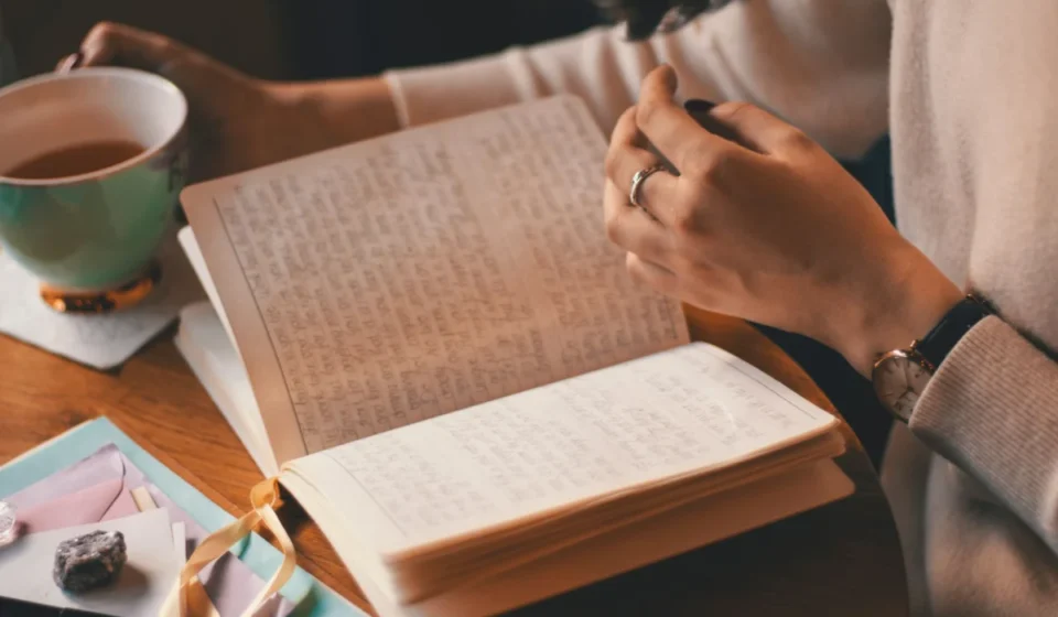 A woman writes in a journal while enjoying a cup of coffee at a wooden table.