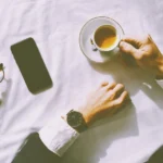 Flat lay of man enjoying espresso with smartphone, watch, and glasses on a table.