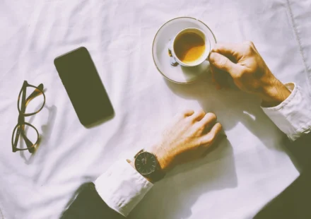 Flat lay of man enjoying espresso with smartphone, watch, and glasses on a table.