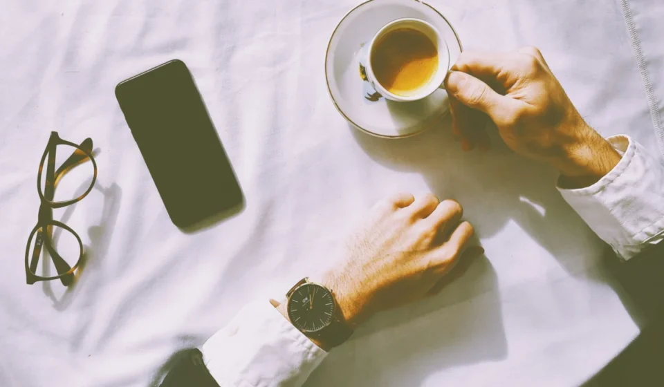 Flat lay of man enjoying espresso with smartphone, watch, and glasses on a table.
