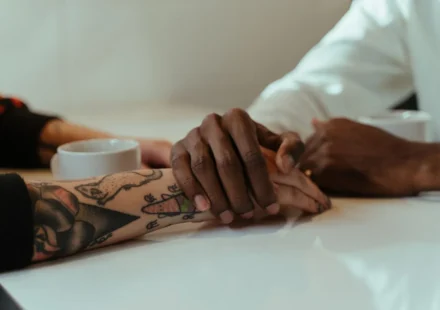Interracial couple holding hands over coffee, showcasing love and connection with tattoos visible.