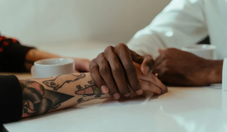 Interracial couple holding hands over coffee, showcasing love and connection with tattoos visible.