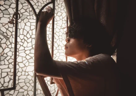Side view of a young man posing thoughtfully by a mosaic glass window with soft light.