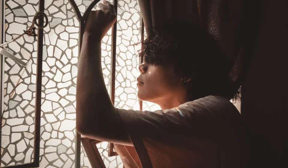Side view of a young man posing thoughtfully by a mosaic glass window with soft light.
